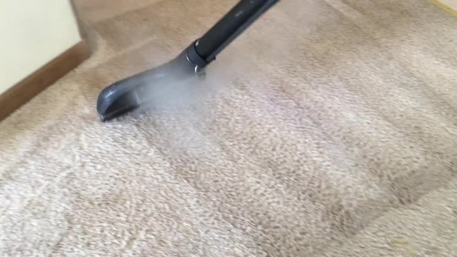 Carpet cleaning professional works wand from above while hot steamy water drives down into surface before extraction thereafter.  