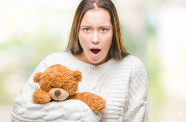 Young caucasian woman holding teddy bear over isolated background scared in shock with a surprise face, afraid and excited with fear expression