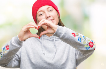 Young caucasian beautiful woman wearing wool cap over isolated background smiling in love showing heart symbol and shape with hands. Romantic concept.