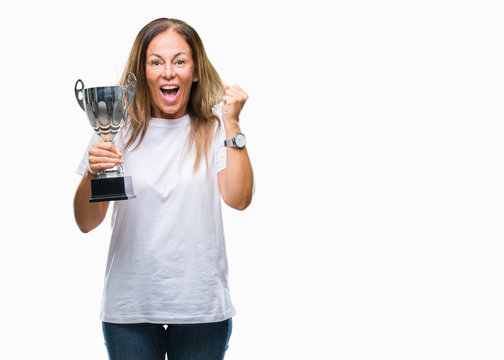 Middle age hispanic winner woman celebrating award holding trophy over isolated background screaming proud and celebrating victory and success very excited, cheering emotion