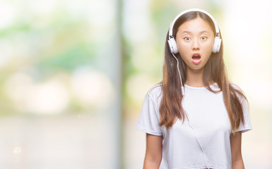 Young asian woman listening to music wearing headphones isolated background scared in shock with a surprise face, afraid and excited with fear expression