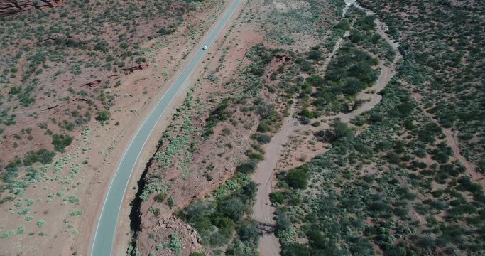 Aerial drone scene of red sandstone cliffs. Flying above ravines and canyons with native vegetation on the top. Road with car crossing landscape. Camera from senital to lateral view