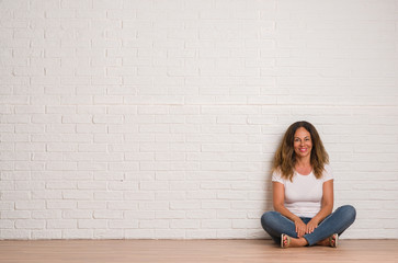 Middle age hispanic woman over white brick wall with a happy face standing and smiling with a...