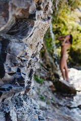 Nude woman on a sunny summer day. A young woman enjoys the freshness and spray of clean water at the waterfall. A woman takes a shower under a waterfall. In the foreground rocks.