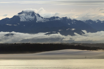 A lone sailboat in a bank of fog below the majestic Olympic mountains
