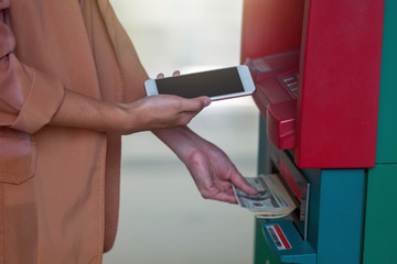 woman using the smart mobile phone for withdrawing in front of the ATM, business Automatic Teller Machine concept