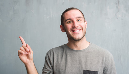 Young caucasian man over grey grunge wall very happy pointing with hand and finger to the side