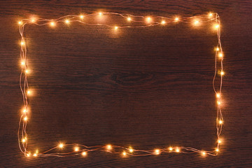 Christmas lights garland border over dark wooden background. Flat lay, copy space.