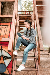 Making notes. Cheerful brunette female sitting on stairs while looking at her gadget