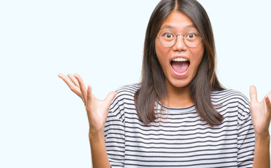 Young asian woman wearing glasses over isolated background celebrating crazy and amazed for success with arms raised and open eyes screaming excited. Winner concept
