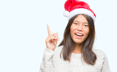 Young asian woman wearing christmas hat over isolated background pointing finger up with successful idea. Exited and happy. Number one.