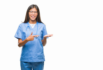 Young asian doctor woman over isolated background amazed and smiling to the camera while presenting with hand and pointing with finger.