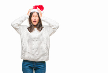 Young asian woman wearing christmas hat over isolated background suffering from headache desperate and stressed because pain and migraine. Hands on head.