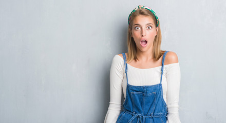 Beautiful young woman standing over grunge grey wall scared in shock with a surprise face, afraid and excited with fear expression