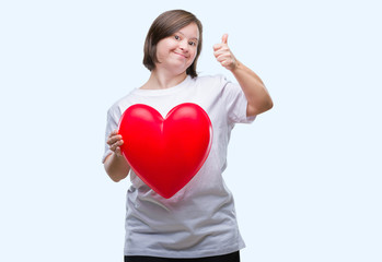 Fototapeta na wymiar Young adult woman with down syndrome holding red heart over isolated background happy with big smile doing ok sign, thumb up with fingers, excellent sign