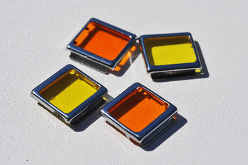 Four square color filters - two yellow and two orange on a white background in a bright sunny day