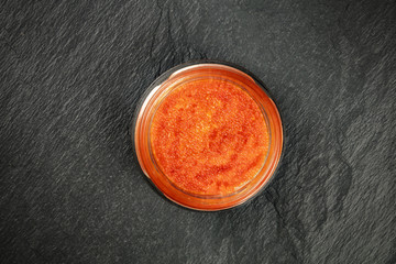 Red fish caviar in a jar, shot from the top on a black background with copyspace