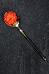 Red fish caviar in a vintage spoon, shot from the top on a black background with copyspace