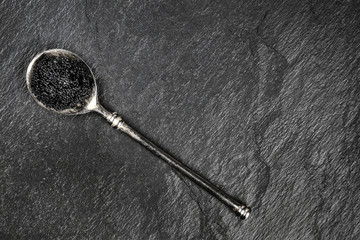 Black fish caviar in a vintage spoon, shot from the top on a black background with copyspace
