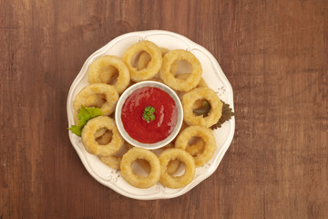 A photo of squid rings with a tomato sauce, shot from the top on a dark rustic wooden background with copy space