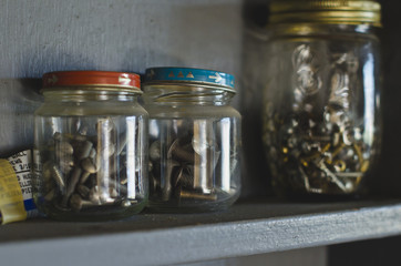 A wooden shelf in the shop with the jars full of screws. 