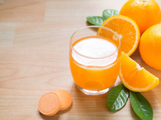 Vitamin c effervescent tablet is dissolving in glass of water w/ bubbles and fresh juicy orange...