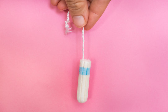 Woman is holding menstruation tampon in hand on pink