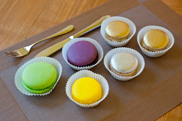 Macaroons of bright different colors in paper forms close-up shot next to cutlery