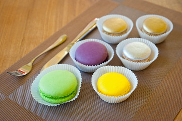 Macaroons of bright different colors in paper forms close-up shot next to cutlery