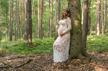 Beautiful pregnant woman in white lace dress in forest