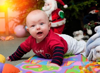 Little baby under Christmas tree, smiling and playing 