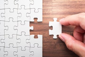 Putting last jigsaw puzzle piece. Solving and completing the task. The correct solution. Assembling white jigsaw puzzle pieces.