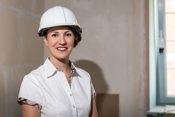 Cute young woman in white construction protection building helmet in unfinished apartment