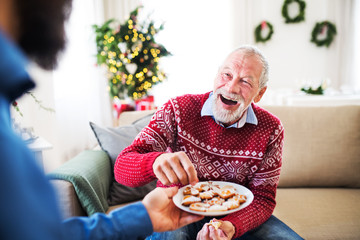 A man giving biscuits to his senior father at home at Christmas time.