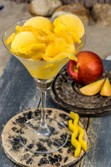 Glass cup with mango peach fruit ice-cream sorbet balls served on stone plank on sandy beach with seashells