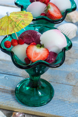 Green glass vintage cups with fruit ice-cream sorbet balls served on blue plank on sandy beach with seashells