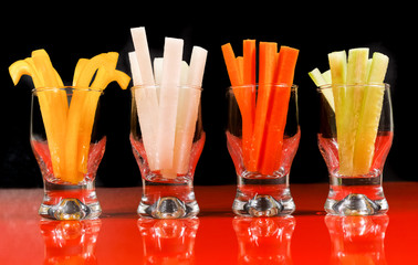 Four types of vegetable sticks, healthy finger food served on red table with reflection