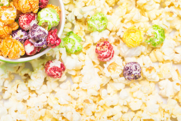 a glass of multi-colored caramel corn against a background of popcorn
