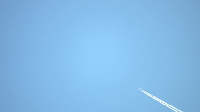 A distant passenger jet with a thick, white contrail flies across the clear, blue, daytime sky above.