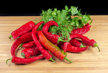 Red chili and greens on wooden surface on black background