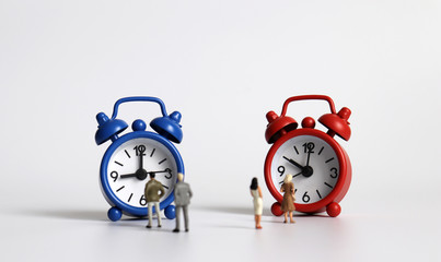 Miniature men and miniature women standing in front of other alarm clocks.