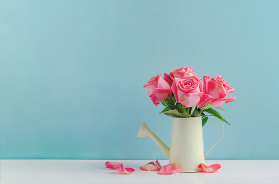 Withered rose flowers at watering can on white and blue wooden background