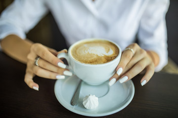 close up hand of woman holding a cup of hot latte in the cafe