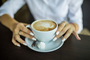 close up hand of woman holding a cup of hot latte in the cafe