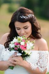 Fototapeta premium Beautiful brunette girl with a bouquet of flowers. Young woman with long curly hair in a white lace dress. Summer female portrait