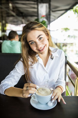 portrait of beautiful charming woman is stirring coffee in cafe and thinking