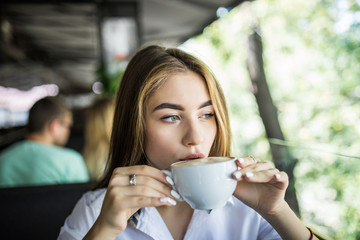 Portrait of beautiful young woman, sitting in a cafe outdoor, drinking coffee