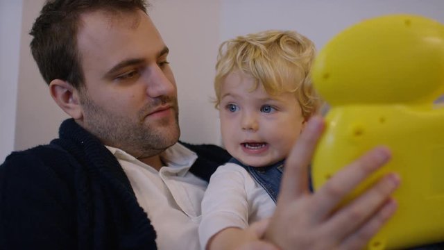 Young father looking at an educational toy with his toddler son, in slow motion 