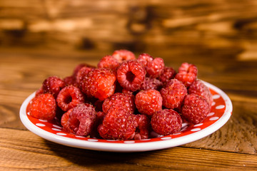 Ceramic plate with ripe raspberries on wooden table