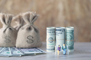Miniature couple standing on the chair and money bag with banknote on wooden background, Save money for prepare in future and retirement concept.